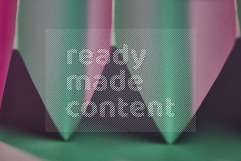 صورة مجردة مقربة تظهر طيات ورقية هندسية حادة بتدرجات اللون الأخضر والوردي