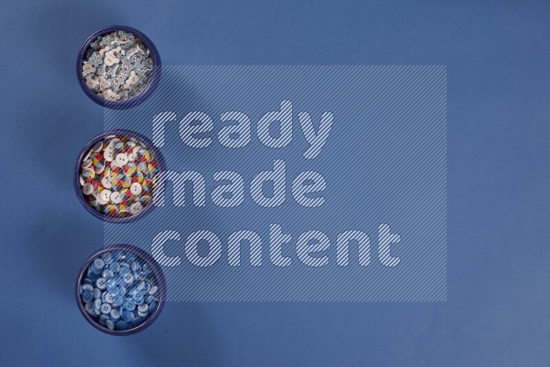 أوعية فخارية متعددة الألوان مليئة بالأزرار الملونة على خلفية زرقاء