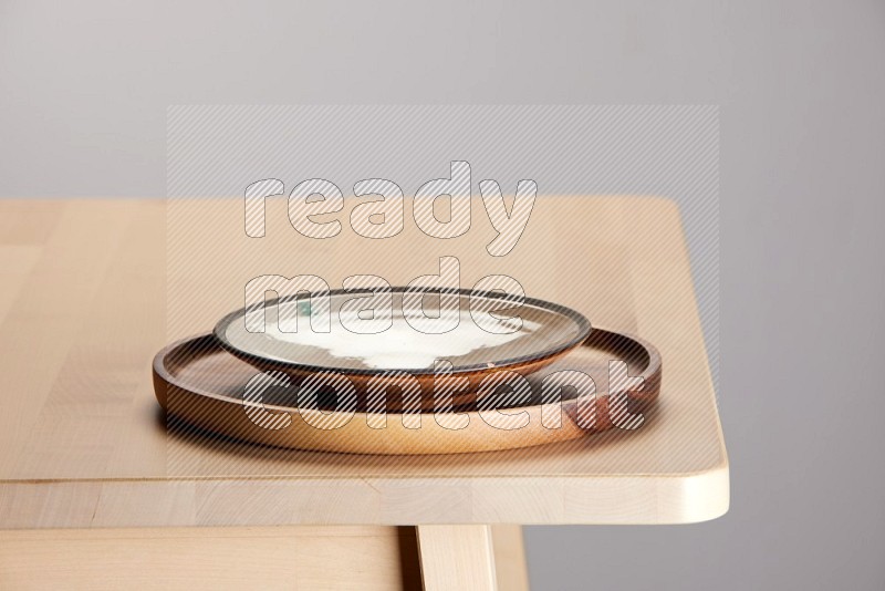 multi-colored pottery Plate placed on a light colored wooden tray on the edge of wooden table