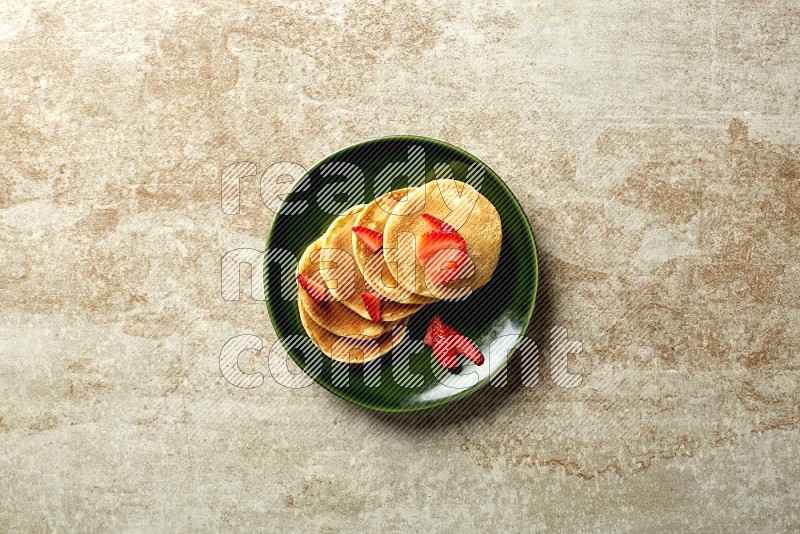Five stacked strawberry mini pancakes in a green plate on beige background