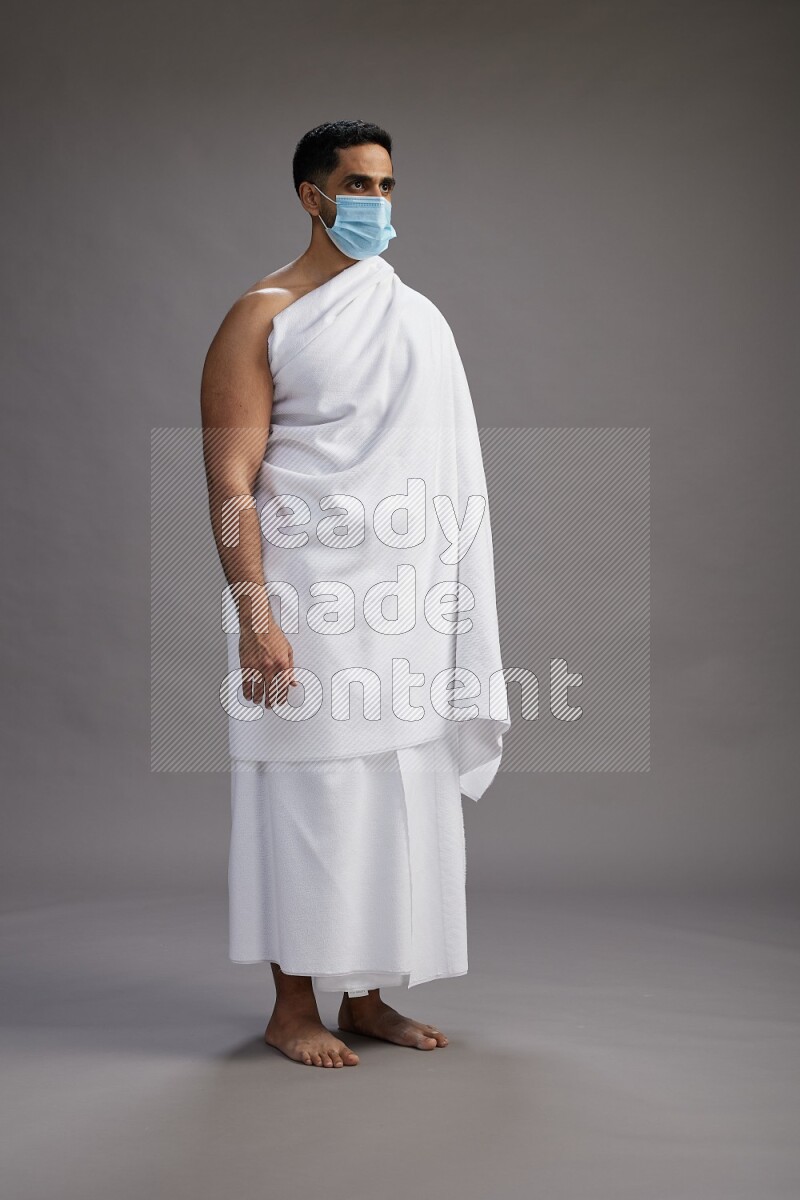 A man wearing Ehram with face mask Standing Interacting with the camera on gray background