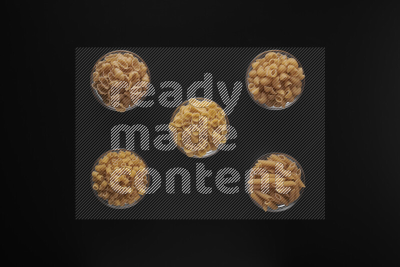 Different pasta types in 5 glass bowls on black background