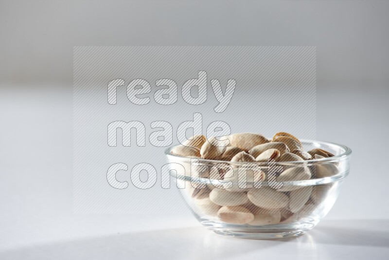 A glass bowl full of pistachios on a white background in different angles