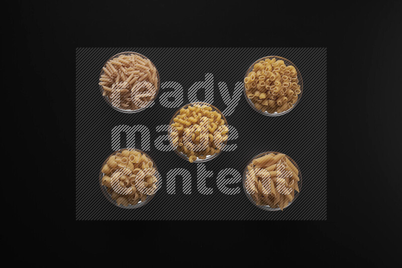 Different pasta types in 5 glass bowls on black background