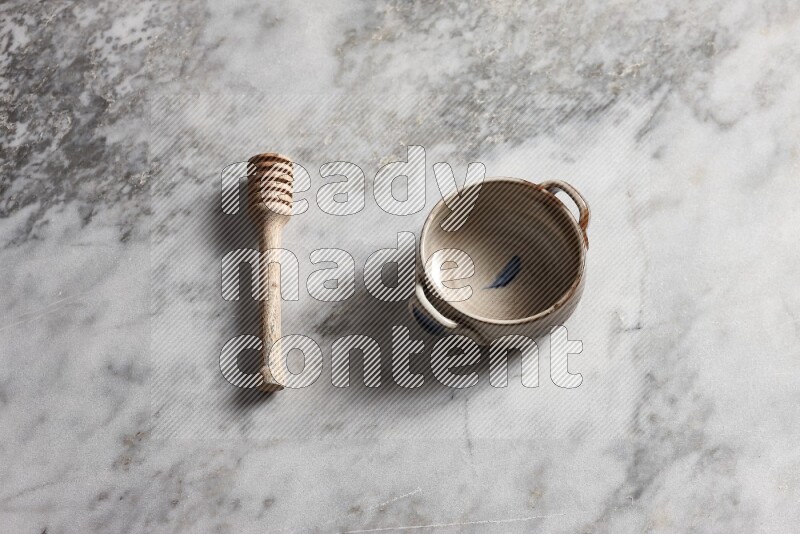 Multicolored pottery bowl with wooden honey dipper on the side on grey marble background