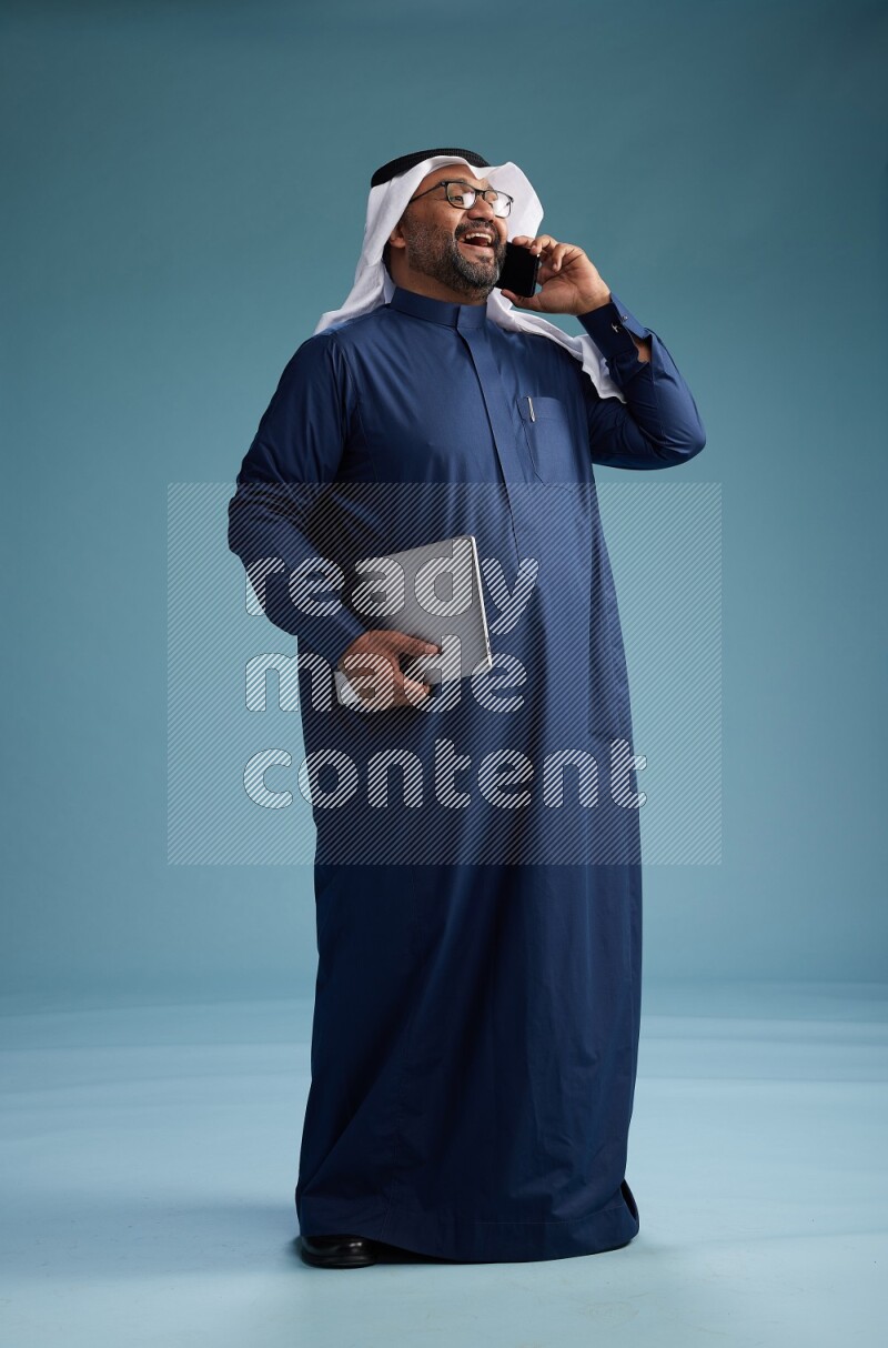 Saudi Man with shimag Standing talking on phone on blue background