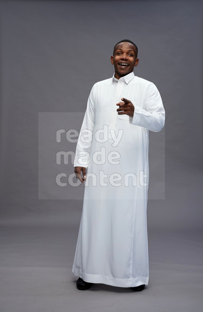 Saudi man wearing thob standing interacting with the camera on gray background