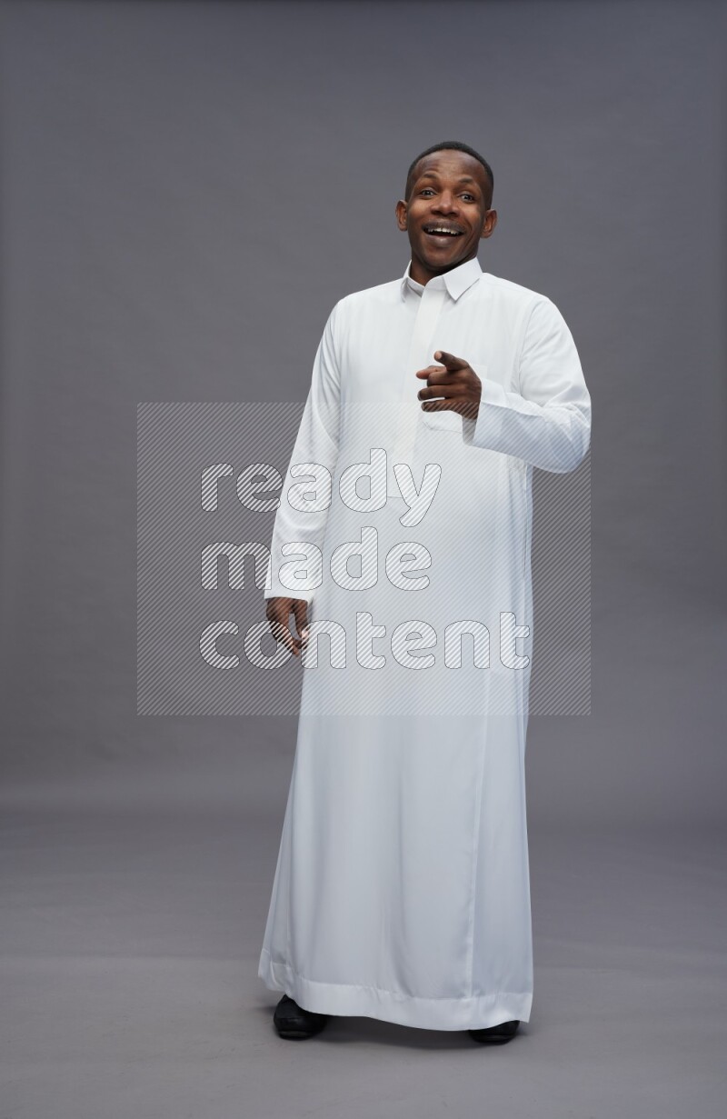 Saudi man wearing thob standing interacting with the camera on gray background