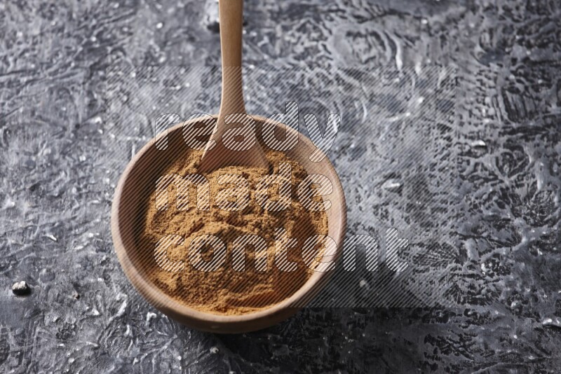 Wooden bowl full of cinnamon powder with a wooden spoon on a textured black background in different angles