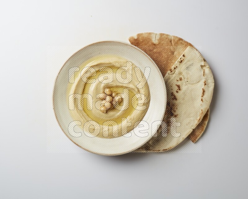 Hummus in a pottry plate garnished with roasted chickpeas on a white background