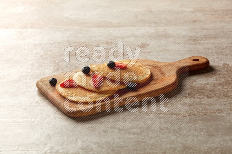 Three stacked mixed berries pancakes on a wooden board on beige background