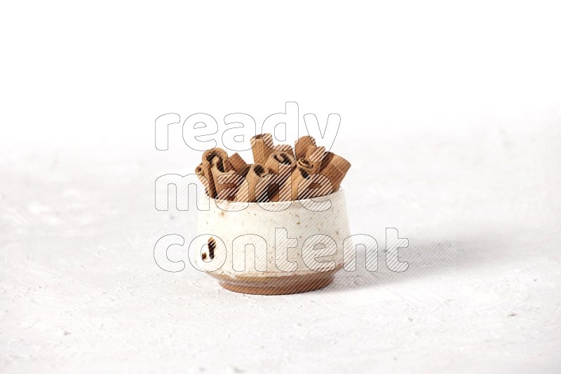 Cinnamon sticks in a beige bowl on a white background