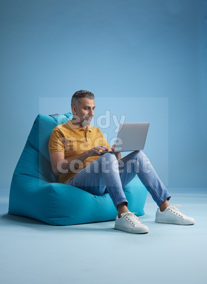 A man sitting on a blue beanbag and working on laptop
