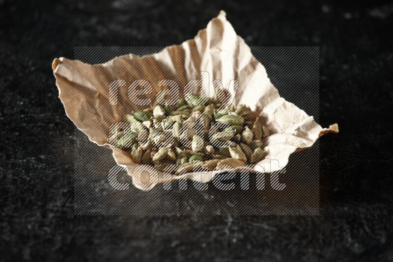 Cardamom seeds in a crumpled piece of paper on textured black flooring