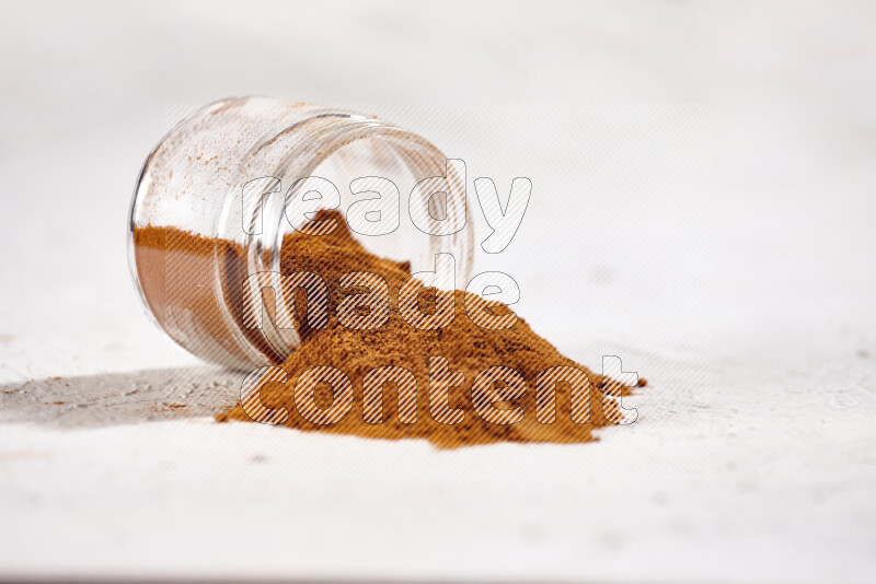 A glass jar full of ground paprika powder flipped with some spilling powder on white background