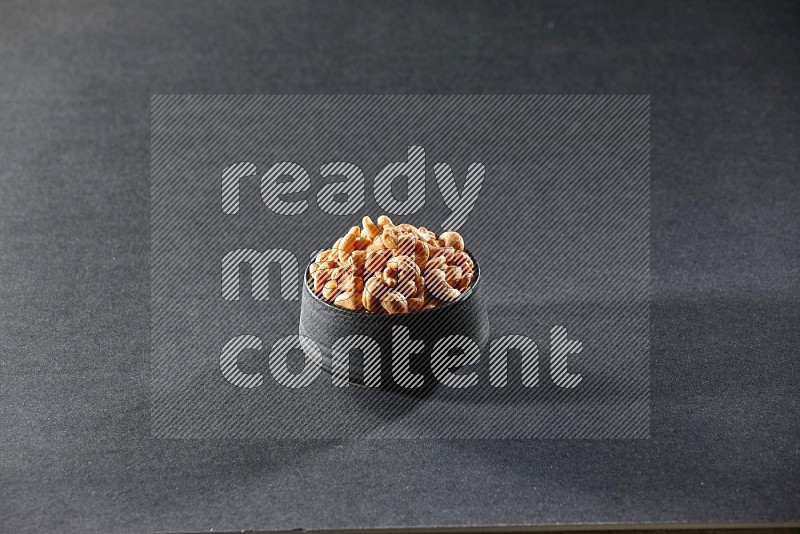 A black pottery bowl full of cashews on a black background in different angles