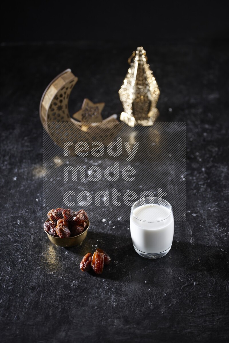 Dates in a metal bowl with milk beside golden lanterns in a dark setup