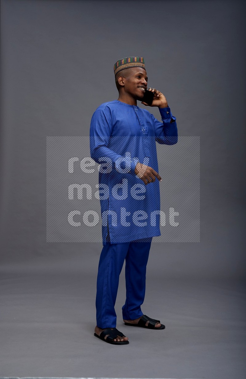 Man wearing Nigerian outfit standing talking on phone on gray background