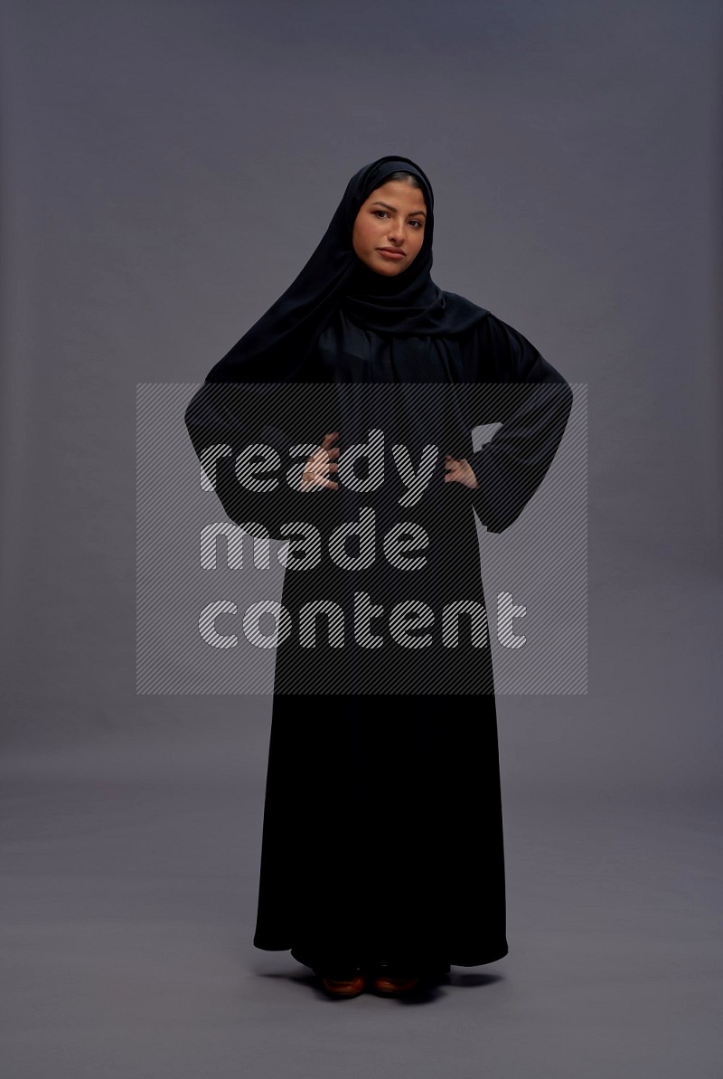 Saudi woman wearing Abaya standing interacting with the camera on gray background