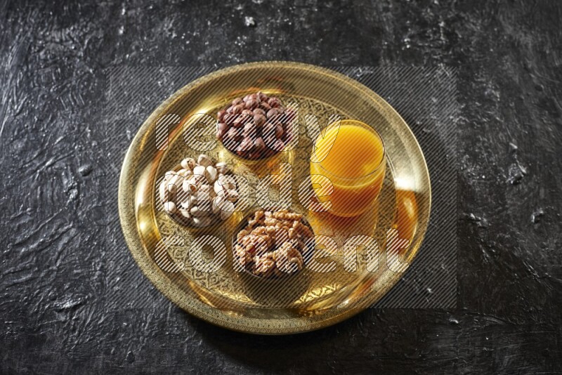 Nuts in metal bowls with qamar eldin on a tray in dark setup