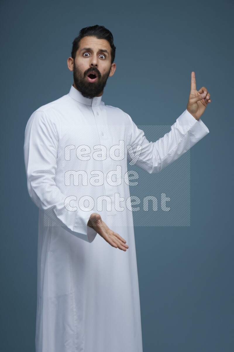 A man pointing in a blue background wearing Saudi Thob