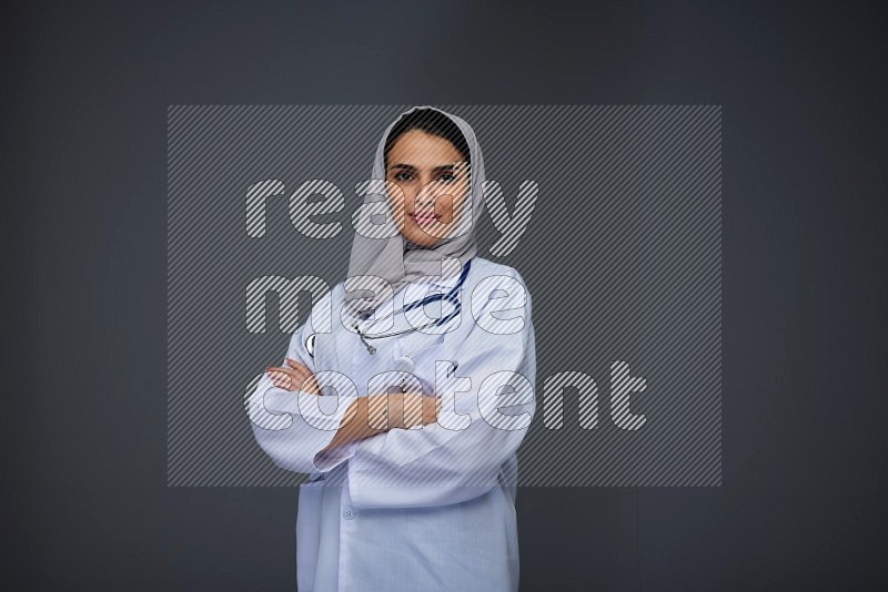 A female doctor wearing a light gray head scarf standing on grey background.