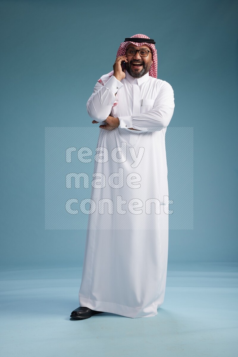Saudi Man with shimag Standing talking on phone on blue background
