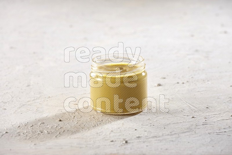 A glass jar full of mustard paste on a textured white flooring