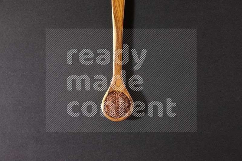 A wooden ladle full of garden cress seeds on a black flooring