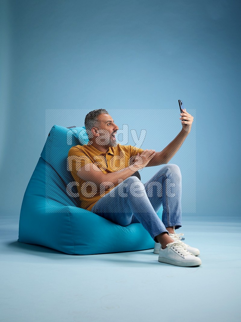 A man sitting on a blue beanbag and taking selfie