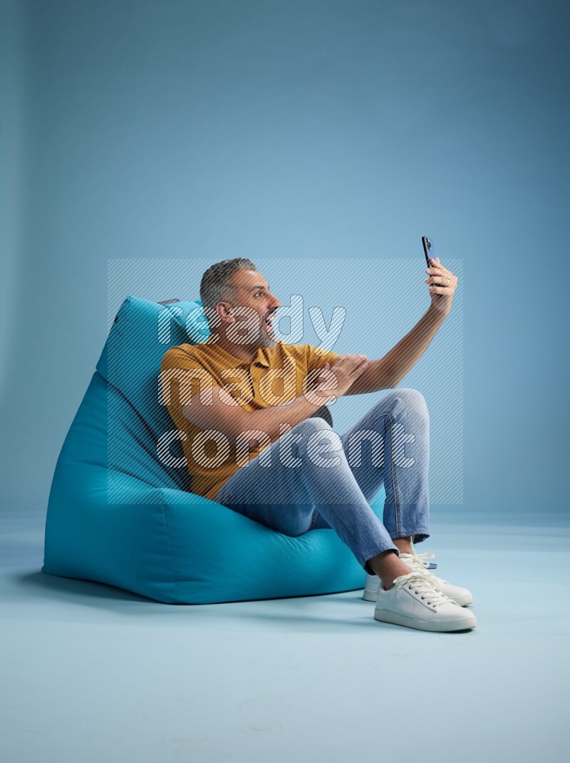 A man sitting on a blue beanbag and taking selfie