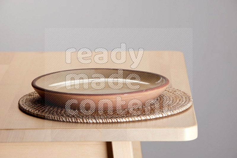 multi-colored pottery Plate placed on a big light colored straw placemat on the edge of wooden table