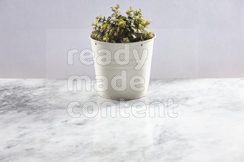 Green artificial plant in white pot on light grey marble background