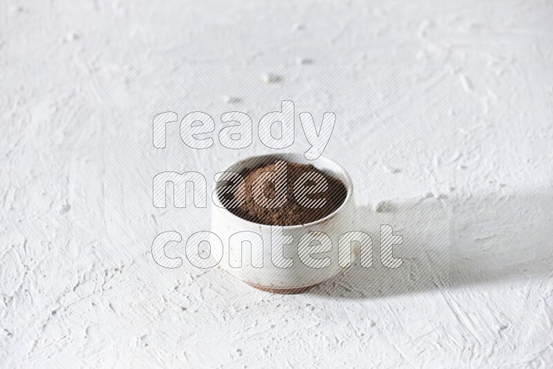 A beige ceramic bowl full of cloves powder on a white flooring