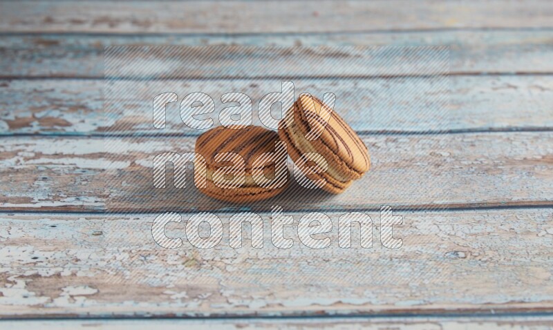 45º Shot of two light brown Almond Cream macarons on light blue wooden background