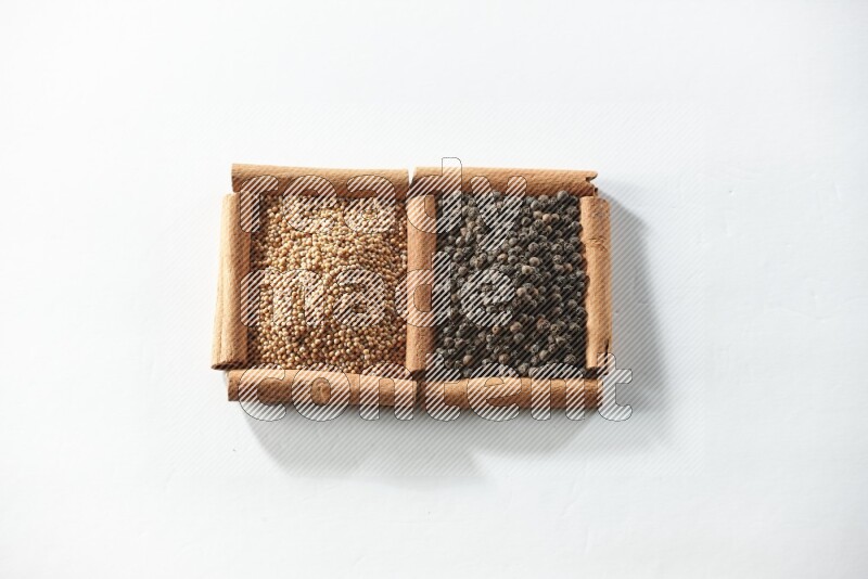 مربعان من أعواد القرفة ممتلئان بحبوب الخردل وحبوب الفلفل الأسود علي خلفية بيضاء