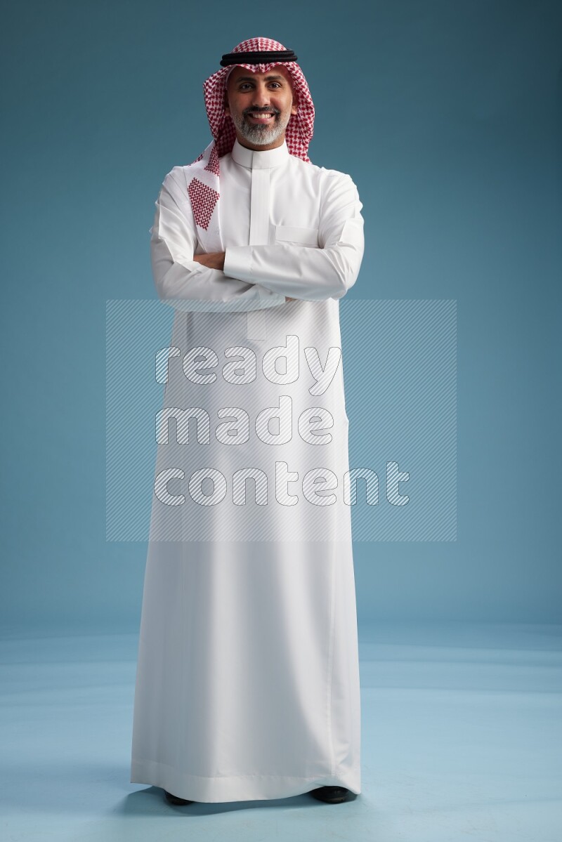 Saudi man wearing thob and shomagh posing to the camera on blue background