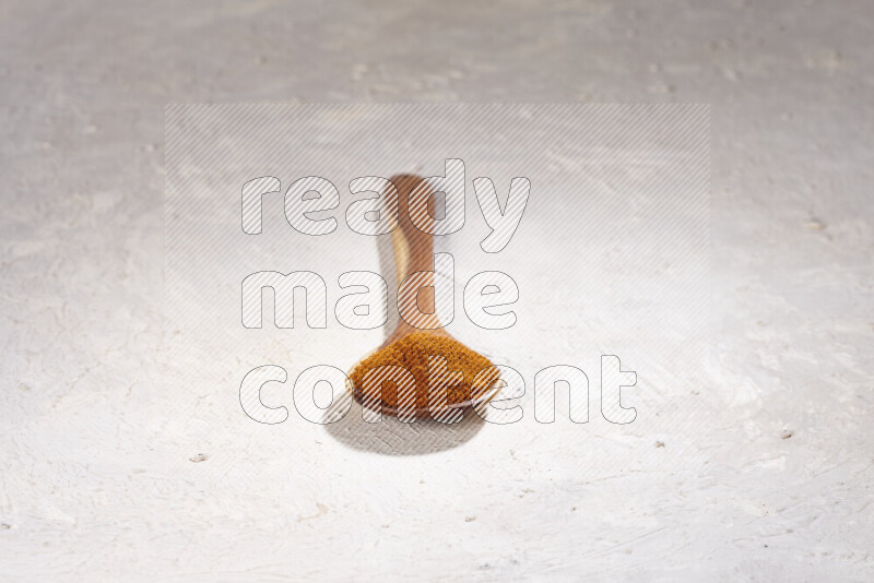 A wooden ladle full of ground paprika powder on white background