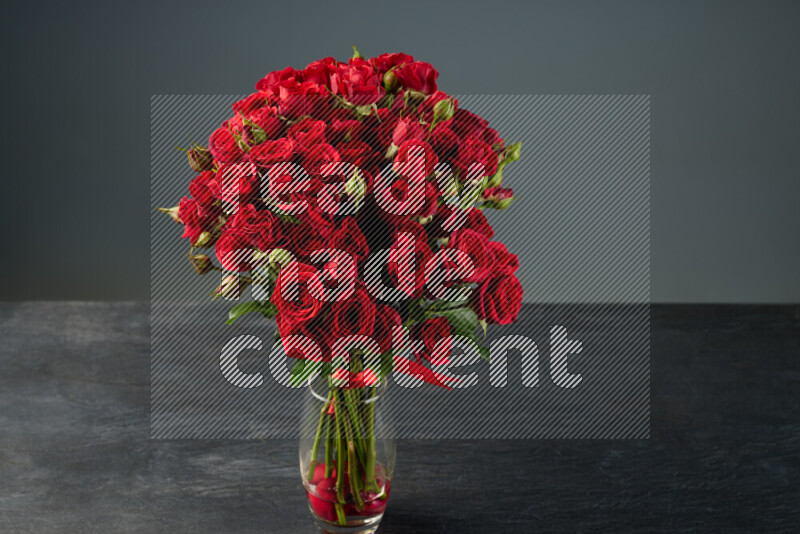 An arrangement of vivid red roses tightly bound with a red ribbon in a glass vase on black marble background