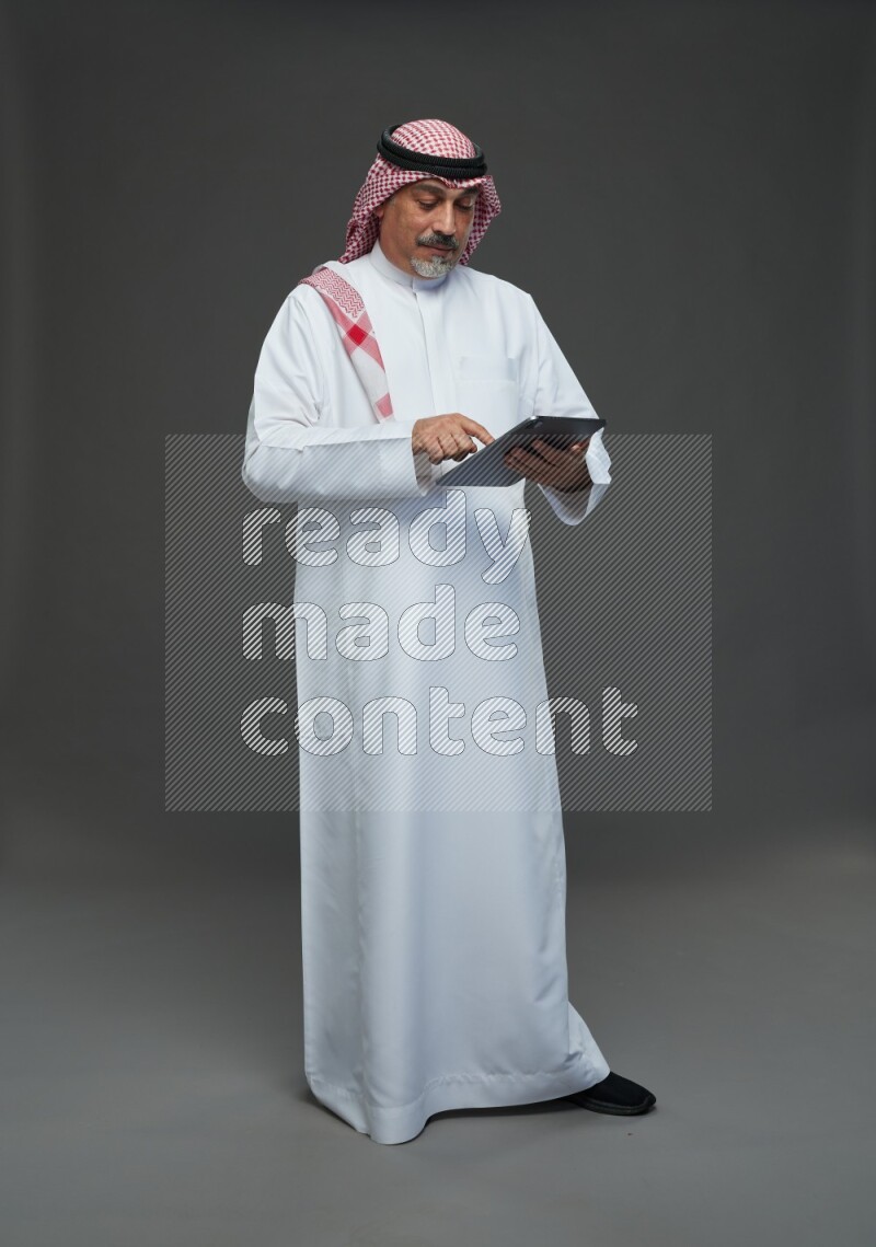 Saudi man with shomag Standing working on tablet on gray background