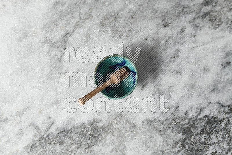 Decorative Pottery Bowl with wooden honey handle in it, on grey marble flooring, Top View