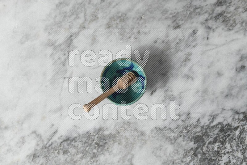 Decorative pottery bowl with wooden honey dipper in it on grey marble background