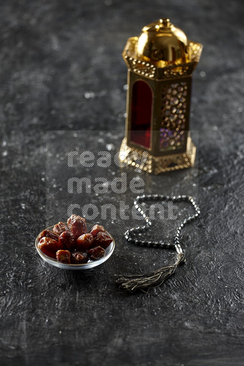 A golden lantern with different drinks, dates, nuts, prayer beads and quran on textured black background