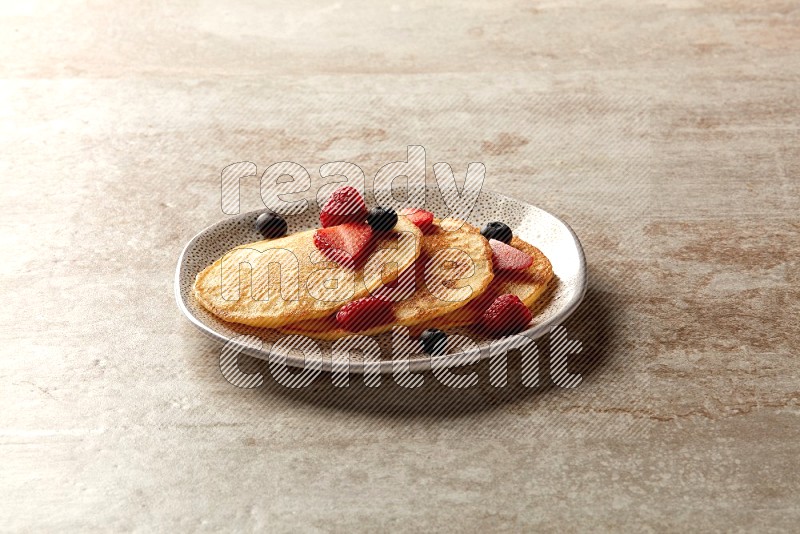 Three stacked mixed berries pancakes in an irregular plate on beige background