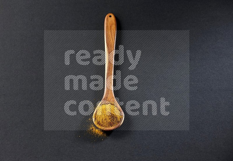 A wooden ladle full of turmeric powder on black flooring
