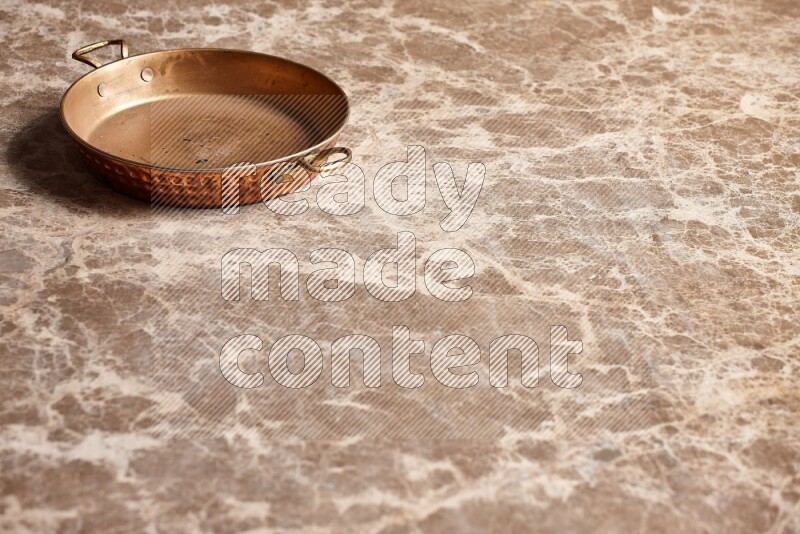 A small copper pan on beige marble background