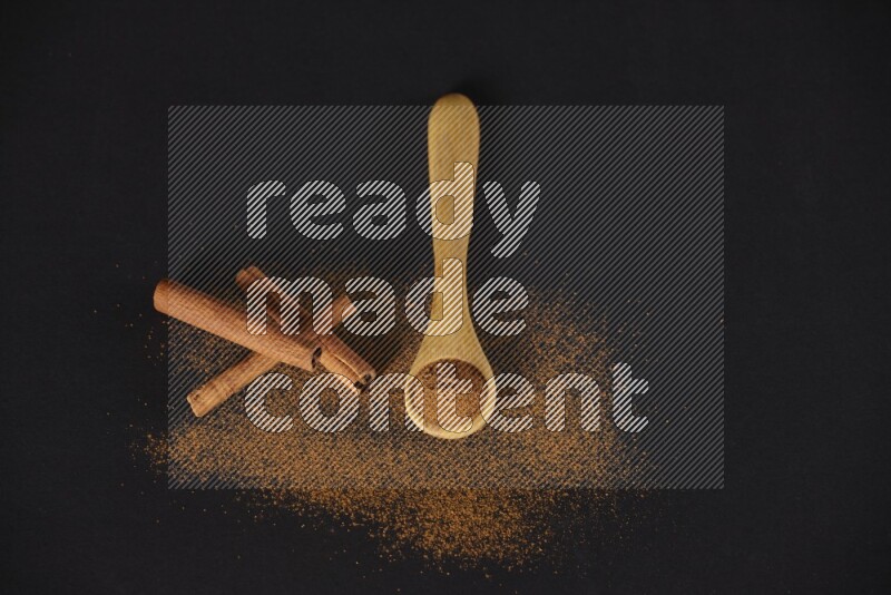 Cinnamon powder in a wooden spoon and cinnamon sticks beside it on black background