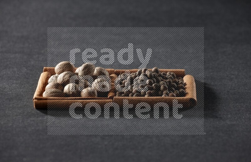 مربعان من أعواد القرفة ممتلئان بجوزة الطيب وحبوب الفلفل الحلو علي خلفية سوداء