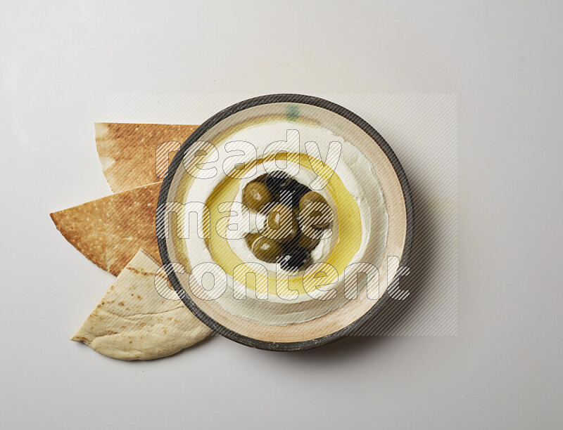 Lebnah garnished with whole black olives in a pottery plate on a white background