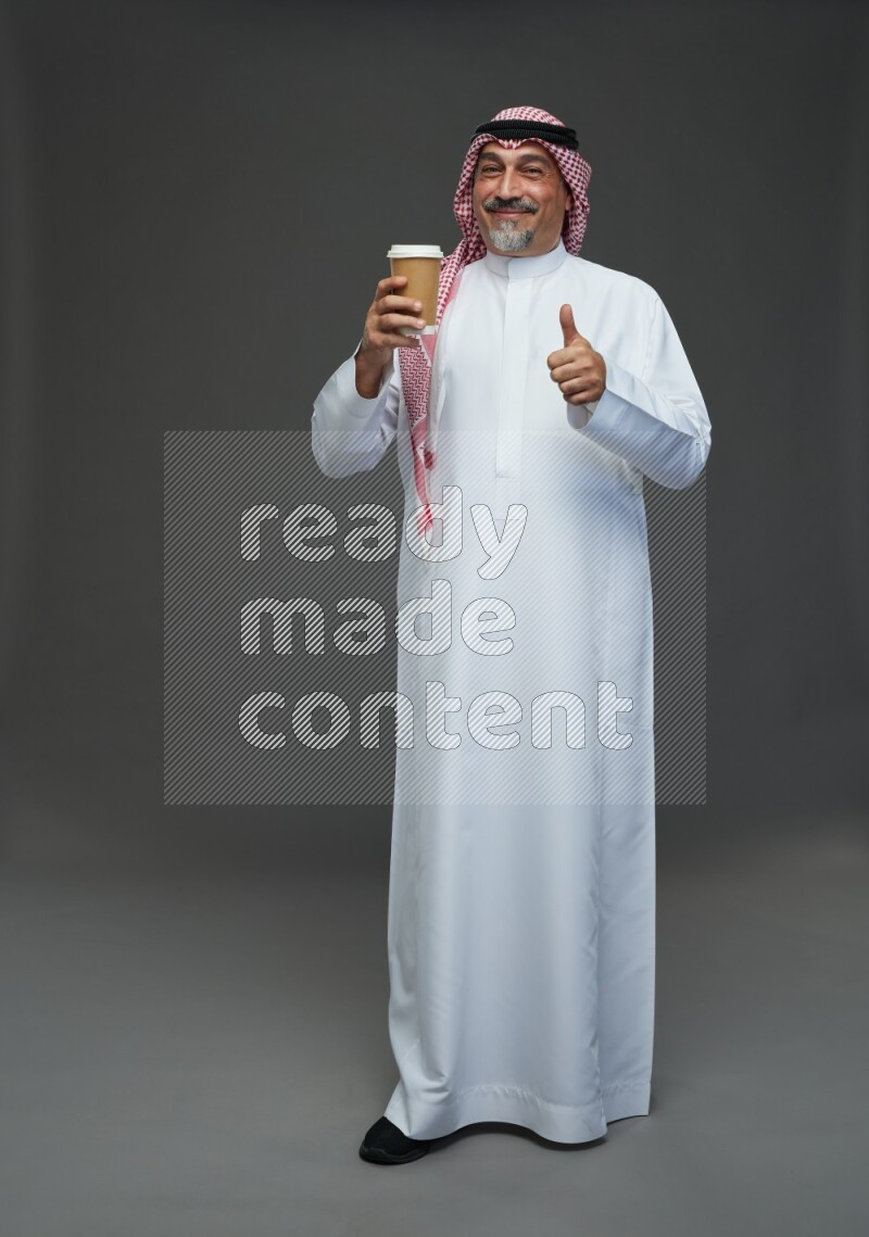 Saudi man with shomag Standing holding paper cup on gray background